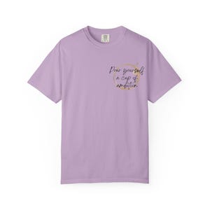 May include: A light purple short-sleeve t-shirt featuring a gold circular coffee ring stain graphic on the left chest. Inside the circle, the black cursive text reads, "Pour yourself a cup of ambition." The shirt has a crew neckline and a standard fit.