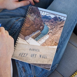 May include: A spiral bound notebook with a photo of the Hoover Dam on the cover. The photo shows the dam and the bridge over the dam. The text on the cover reads "Danger Keep Off Wall".