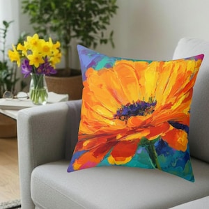 May include: Square throw pillow featuring a vibrant, impressionistic painting of a large orange and yellow flower with a dark blue center. The artwork has bold brushstrokes and is set against a teal and blue background.