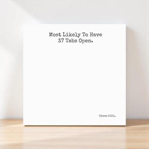 May include: A white square canvas with the text "Most Likely To Have 37 Tabs Open" in black, with "Since 2021" below. The canvas is set against a white wall and a wooden surface.