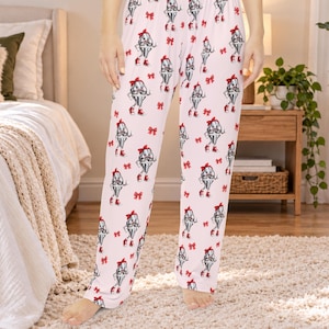 May include: Light pink pajama pants featuring an all-over repeating pattern of cartoon ice cream cones with mustaches and red bows, interspersed with small red bow icons. The pants have a relaxed fit with a straight leg and an elasticized waistband.