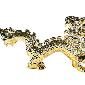Può includere: Una statuetta di drago dorata con dettagli intricati. Il drago è arrotolato su se stesso con la testa alzata e la coda avvolta attorno al suo corpo. La statuetta è realizzata in un materiale lucido e metallico.