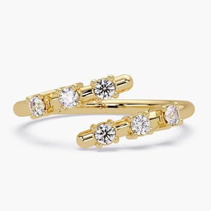 Op de afbeelding: Een goudkleurige ring met een wikkelontwerp. De ring heeft vijf heldere, rond geslepen edelstenen. De edelstenen zijn gezet in een prong setting. De ring staat tegen een witte achtergrond.