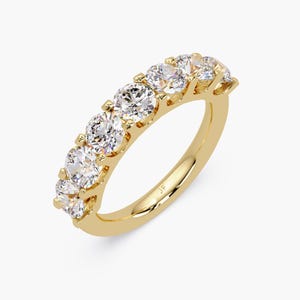 May include: A gold band ring featuring seven round, clear gemstones. The ring has a polished finish and is set with the gemstones evenly spaced along the top of the band. The ring is set against a white background.