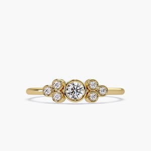 Puede incluir: Un anillo de oro con siete diamantes redondos. El diamante central, más grande, está rodeado por seis más pequeños. El anillo tiene una banda delgada y pulida y un aspecto brillante.