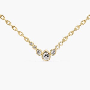 Puede incluir: Un delicado collar de oro con una serie de diamantes brillantes. El collar tiene un colgante central en forma de lágrima, flanqueado por diamantes redondos y en forma de lágrima más pequeños. La cadena es un diseño de eslabones de oro delicado.