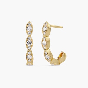 Può includere: Orecchini dorati con una serie di castoni a forma di marquise, ognuno ornato da una scintillante pietra preziosa bianca. Gli orecchini hanno un design a perno e chiusura, che mostra uno stile delicato e ornato.