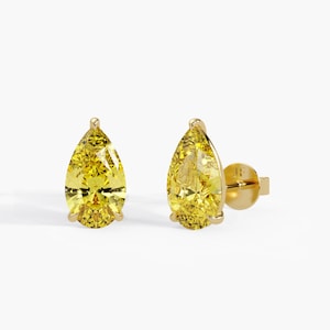 May include: A pair of stud earrings featuring pear-cut yellow gemstones set in polished gold metal. Each earring has a pointed top and a rounded base, secured with a gold post backing that displays the initials JF engraved on the flat circular surface.