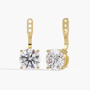 May include: A pair of gold earring jackets featuring a round, clear, faceted gemstone set in a four-prong setting. Each jacket has a vertical post with three circular adjustment holes and the letters JF engraved on the gold stem above the stone.