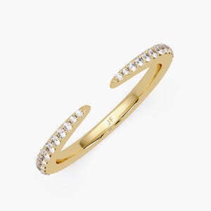 May include: A gold-coloured open ring featuring a line of small, clear gemstones along the outer edges. The ring has a split design, with the ends curving away. The initials "JF" are engraved inside the ring. A piece of jewellery.
