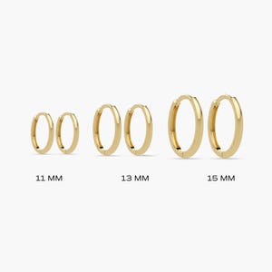 May include: Four pairs of gold hoop earrings in varying sizes: 11 mm, 13 mm, and 15 mm. The earrings are displayed on a white background. The earrings are a classic, minimalist design.
