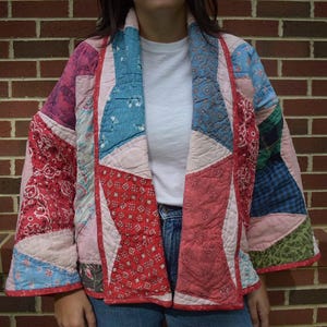 May include: A patchwork jacket in a variety of colors, including red, pink, blue, and green. The jacket has a quilted design and is made of different patterned fabrics. The jacket is open in the front and has long sleeves.