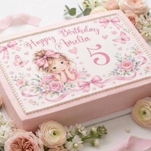 Peut inclure: Un gâteau rectangulaire rose avec une décoration comestible portant l'inscription Happy Birthday Amelia et le chiffre 5. Le motif présente une illustration de fille avec un nœud rose, des papillons, des fleurs et des rubans.