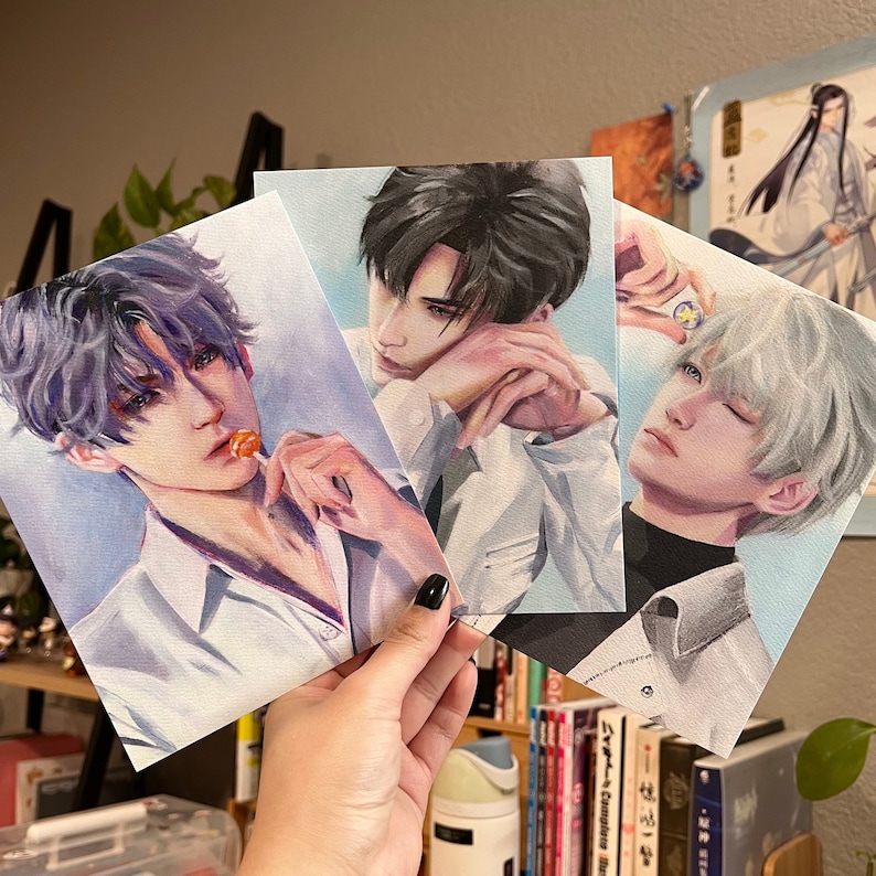 May include: Three portrait prints of male figures with varying hair colours. One holds a lollipop, another rests his chin on his hand, and the third has a ring on his finger. Each is wearing a white shirt. The art style is painterly.