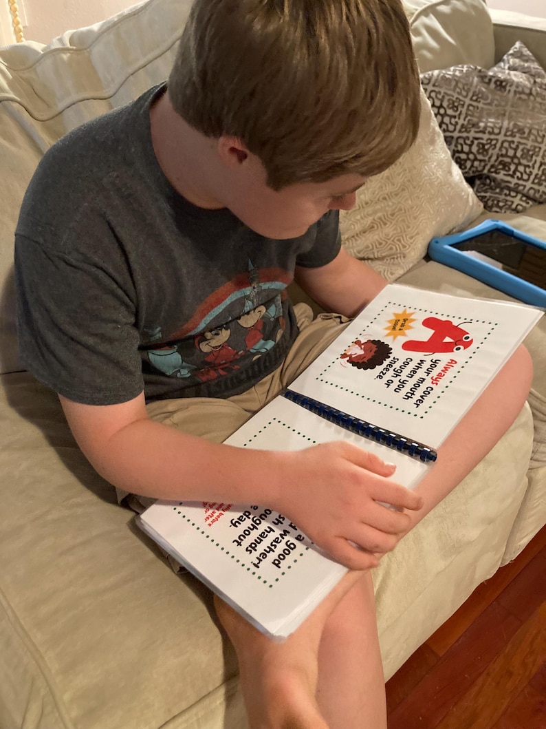 Op de afbeelding: Een jong persoon zit op een bank en leest een boek met een rood nummer vier op de omslag. Het boek heeft de tekst "Bedek altijd je mond wanneer je hoest of niest. Een goede wassen! Was je handen de hele dag door."