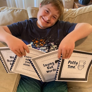 Op de afbeelding: Een jong persoon houdt vier sociale verhalenboeken vast. De boeken zijn getiteld "No Run Away", "Every Net Time Alone", "Saying Bad Words" en "Potty Time".