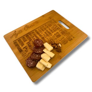 May include: A wooden cutting board with a handle, engraved with the words "Ayiti CherT" and a list of words in French and Creole. The board has a selection of sliced salami, cheese cubes, and almonds on top.