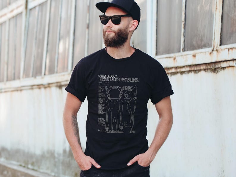 K&ouml;nnte beinhalten: Schwarzes T-Shirt mit dem Text "ASK ME ABOUT KENTUCKY GOBLINS" und einer Goblin-Zeichnung. Die Person tr&auml;gt eine Sonnenbrille und eine schwarze Kappe.