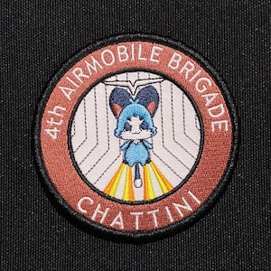 Può includere: Una toppa ricamata marrone e bianca con il testo "4th Airmobile Brigade Chattini" in un cerchio. La toppa presenta un personaggio dei cartoni animati blu e bianco con un disco volante.