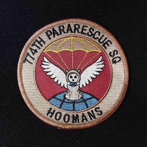 May include: A tan and brown embroidered patch with the text "774th Pararescue Sq" and "HOOMANS" around a red circle with a white owl wearing a blue bow tie and a parachute above it.