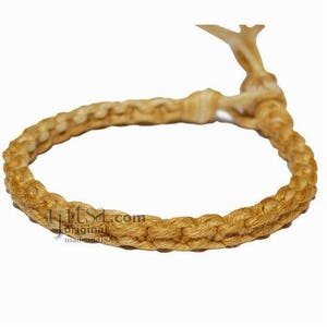 May include: A braided bracelet made of natural beige colored cord. The bracelet is tied with a simple knot.