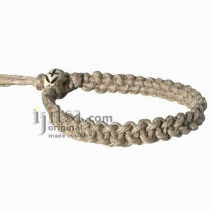 May include: A beige hemp bracelet with a white bead featuring a black design. The bracelet is made with a braided hemp cord.
