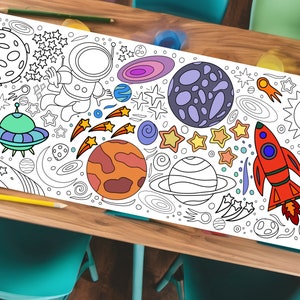 以下が含まれることがあります： 惑星、星、ロケット、宇宙飛行士が描かれた白黒の宇宙をテーマにした塗り絵のテーブルランナー。ランナーは、青い椅子が2脚とピンクの椅子が1脚置かれた木製のテーブルの上に置かれています。