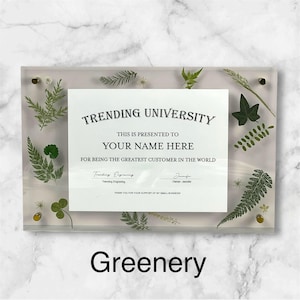 Puede incluir: Placa acr&iacute;lica transparente con el texto "TRENDING UNIVERSITY" y "YOUR NAME HERE". La placa est&aacute; decorada con vegetaci&oacute;n prensada y herrajes dorados. La palabra "Greenery" est&aacute; en la parte inferior.