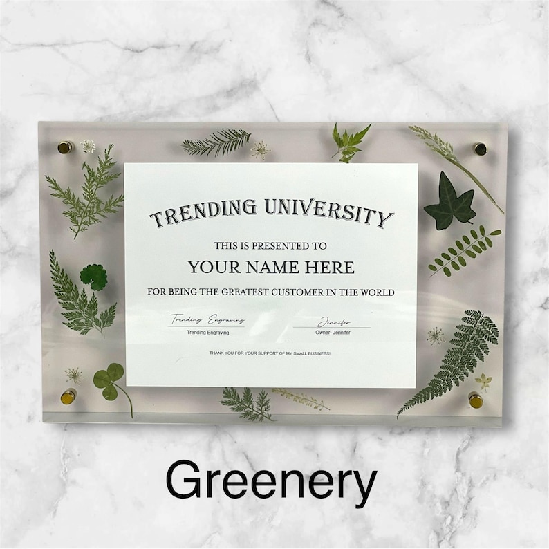 Puede incluir: Placa acr&iacute;lica transparente con el texto "TRENDING UNIVERSITY" y "YOUR NAME HERE". La placa est&aacute; decorada con vegetaci&oacute;n prensada y herrajes dorados. La palabra "Greenery" est&aacute; en la parte inferior.