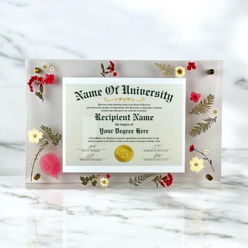 Puede incluir: Un marco acr&iacute;lico transparente contiene un diploma, adornado con flores y follaje secos. El diploma dice "Name Of University" y "Recipient Name" con la informaci&oacute;n del t&iacute;tulo. Herrajes dorados aseguran el marco.