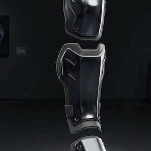 May include: Black protective armor set, including knee and shin guards. The pieces are made of a dark, reflective material with a matte black trim. The design features a segmented construction with visible rivets.