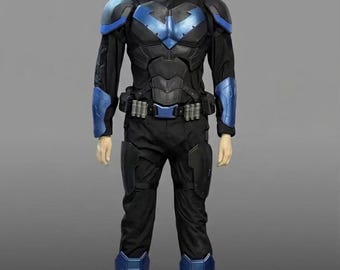 May include: A full-body costume featuring a black fabric jumpsuit with molded black and metallic blue armor plating on the shoulders, chest, forearms, thighs, and shins. It includes a utility belt and a black fabric head mask covering the face.
