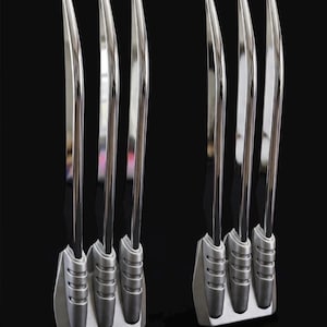 May include: Two sets of three silver-colored metal claw props, each featuring long, curved, reflective blades attached to a textured, matte gray base. The text COSPLAY CASSANOVA is visible in the bottom right corner of the image.