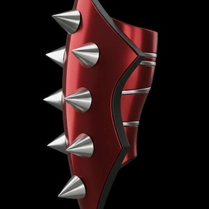 May include: A red arm guard with silver spikes and trim. The guard has a glossy finish and a black border. The design features multiple silver spikes along the outer edge and silver bands. The background is black.