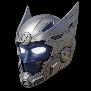 May include: A futuristic silver and blue helmet with glowing white eyes and the letter "X" on the forehead. The helmet has a detailed, mechanical design with angular shapes and ear-like protrusions, set against a black background.