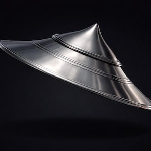 Może przedstawiać: Srebrny kapelusz o futurystycznym wyglądzie, z stożkowym wierzchołkiem i szerokim, zakrzywionym rondem. Kapelusz ma warstwową konstrukcję z poziomymi grzbietami, co nadaje mu elegancki, nowoczesny wygląd. Tło jest czarne.