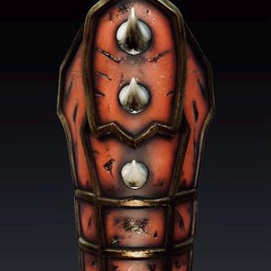 May include: A forearm guard featuring a weathered orange surface with dark distressed markings and a metallic bronze-toned frame. The piece is adorned with three prominent, sharp, conical white spikes arranged vertically along the center.