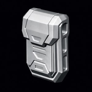 May include: A silver-colored, geometric-shaped object with a futuristic design. The object has a rectangular body with a hinged top and a series of rectangular cutouts on the side. The surface has a metallic sheen, and the overall aesthetic is modern and industrial.