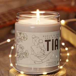 May include: A brown glass candle with a white label that says "Huele a que vas a ser Tia" and features a line drawing of a woman holding a baby. The candle is sitting on a wooden coaster.