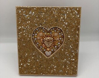 May include: A gold heart-shaped wall decor with a beaded texture and a smaller heart design in the center. The heart is surrounded by smaller gold beads.