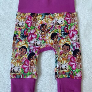 May include: Baby pants with a vibrant floral print featuring cartoon characters, flowers, and animals in shades of pink, yellow, and green. The waistband and cuffs are a solid magenta color.
