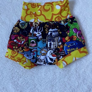 Könnte beinhalten: Gelbe und schwarze Stoff-Baby-Blümchen mit einem bunten Druck verschiedener Comicfiguren, darunter Mickey Mouse, Winnie Puuh und R2-D2.