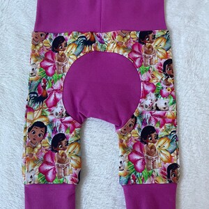 May include: Baby pants with a vibrant floral print featuring cartoon characters and flowers in shades of pink, yellow, and green. The pants have a solid magenta waistband and cuffs.