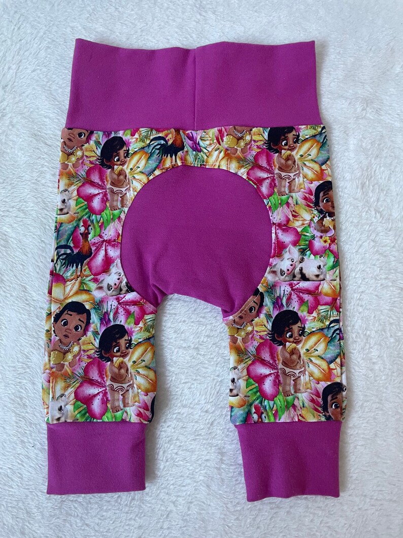 May include: Baby pants with a vibrant floral print featuring cartoon characters and flowers in shades of pink, yellow, and green. The pants have a solid magenta waistband and cuffs.