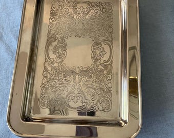 May include: A silver serving tray with ornate engraved designs and two handles. The tray is rectangular and has a polished finish.
