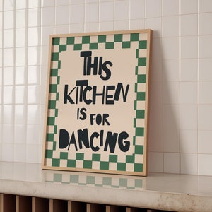 May include: A framed print with a green and white checkered border. The print says "This Kitchen is for Dancing" in black lettering.