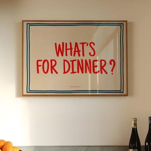 May include: A kitchen scene featuring a framed print with the text "WHAT'S FOR DINNER?" in red. A terracotta bowl filled with oranges sits on a marble countertop, with additional oranges scattered nearby. Two wine bottles are also visible.