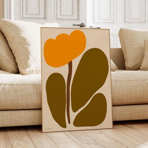 Peut inclure: Impression d'art abstrait repr&eacute;sentant une fleur stylis&eacute;e avec des p&eacute;tales orange et des feuilles vertes. L'impression est encadr&eacute;e et accroch&eacute;e &agrave; un mur dans un salon.