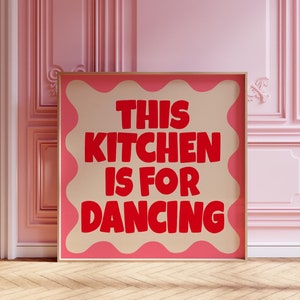 May include: A framed print with a pink background and a wavy border. The text "This Kitchen Is For Dancing" is written in red letters.
