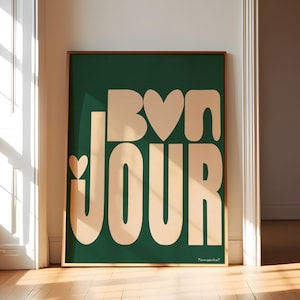 May include: A framed print with a green background and the words "Bon Jour" in a peachy-pink color. The letters are stylized and have hearts incorporated into the design.